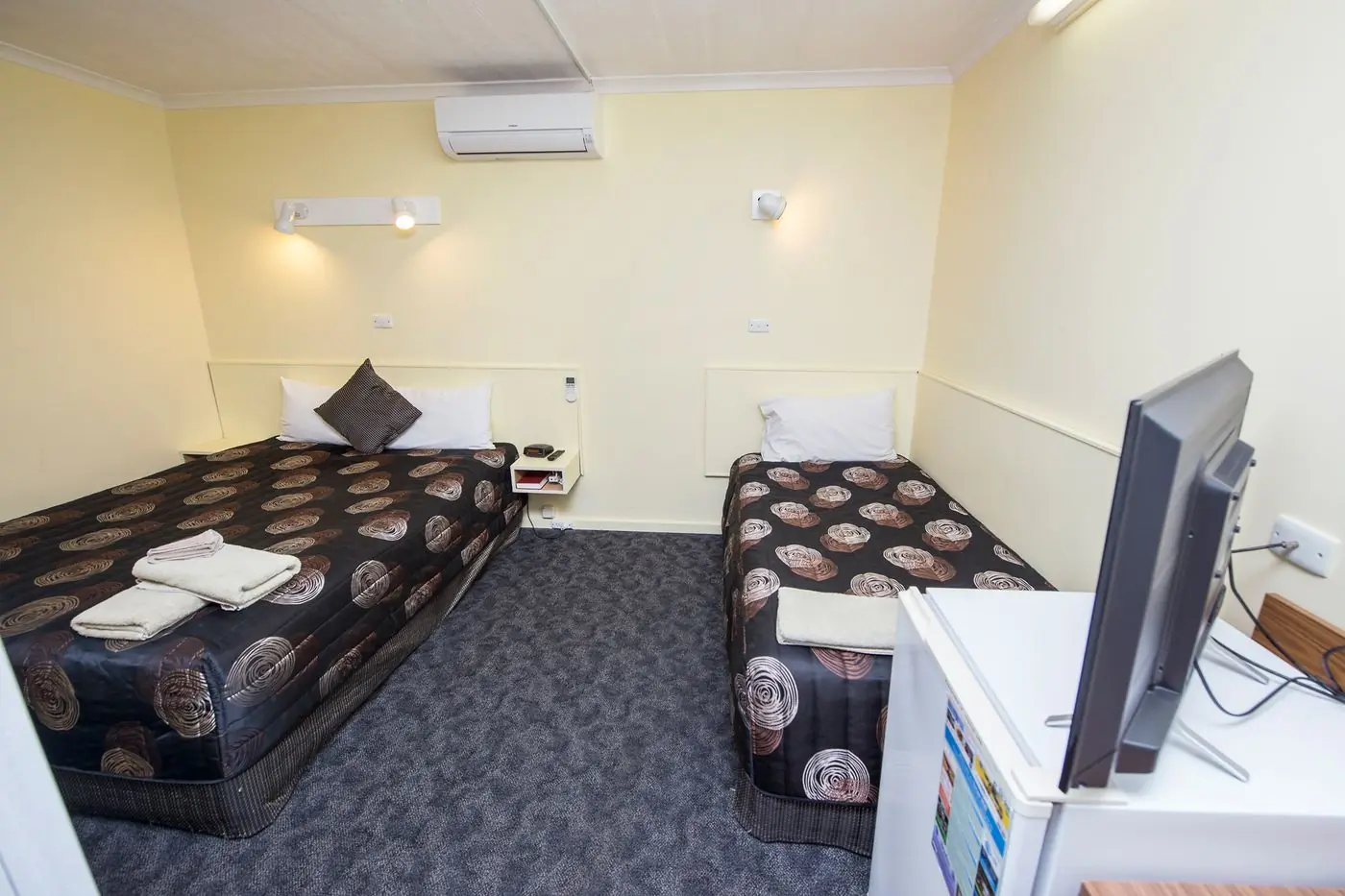 A room with a queen bed and a single bed, and a wall-mounted television