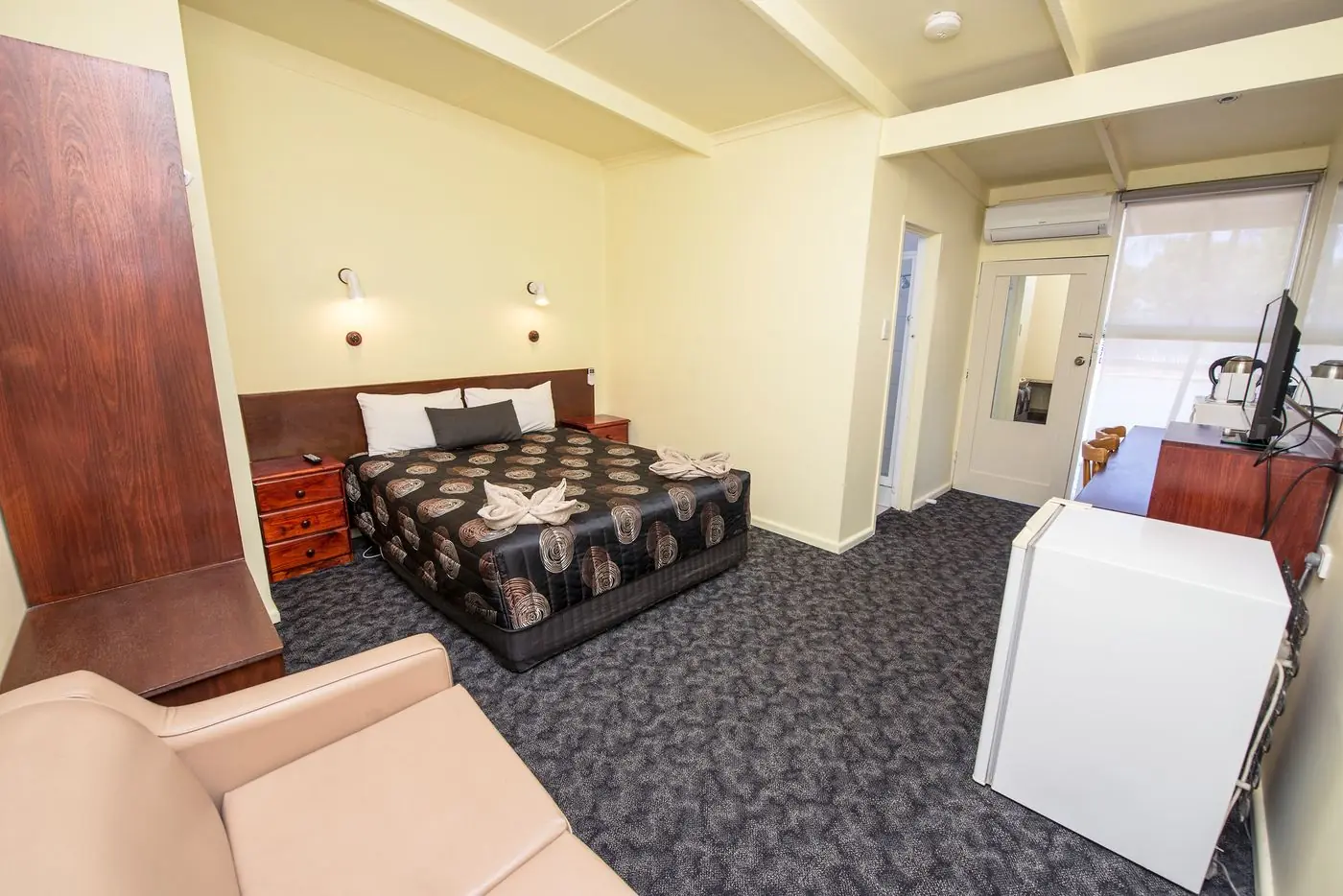 A queen room with a sofa, bar fridge and ensuite door